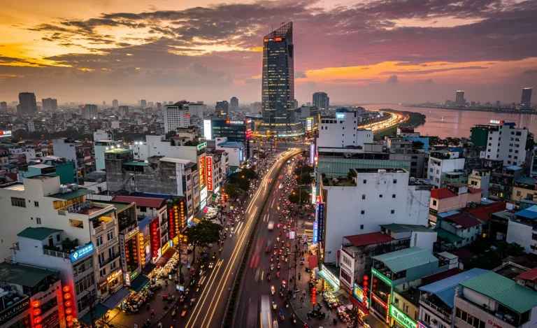 Vue aérienne de Ho Chi Minh-Ville au crépuscule avec la tour Bitexco, des rues animées de scooters et des lanternes lumineuses.
