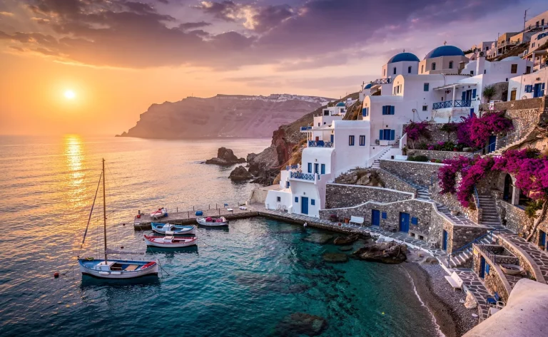 Côte grecque au coucher du soleil avec des eaux claires, un village blanc sur la colline et des barques dans le port.
