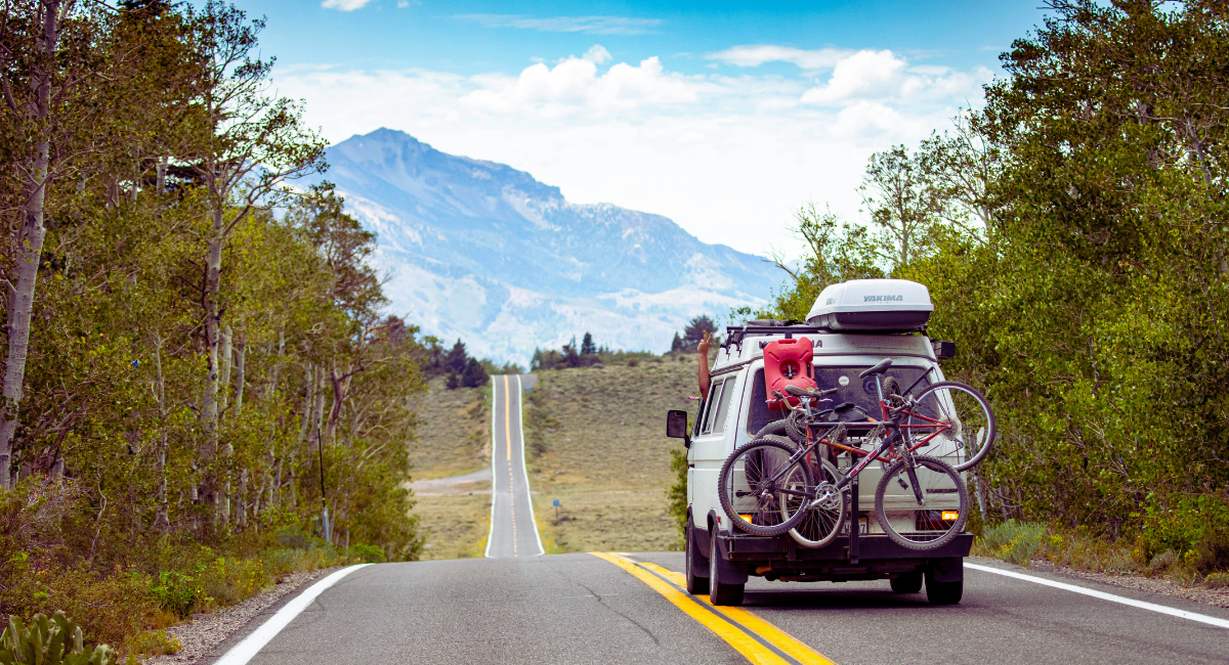 Van aménagé avec vélos sur route panoramique bordée d'arbres en direction des montagnes