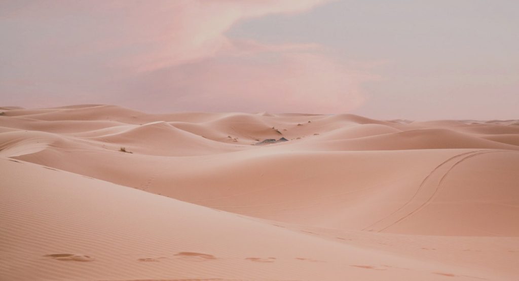Vastes dunes de sable du désert du Sahara au Maroc au crépuscule, avec des empreintes de pas et un ciel rose et mauve