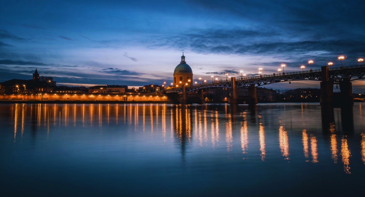 Vue nocturne de Toulouse avec le pont Saint-Pierre et le dôme de La Grave se reflétant dans la Garonne