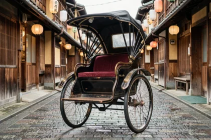 Pousse-pousse traditionnel japonais jinrikisha en bois laqué noir garé dans une ruelle historique de Kyoto avec des maisons machiya en bois et des lanternes en papier